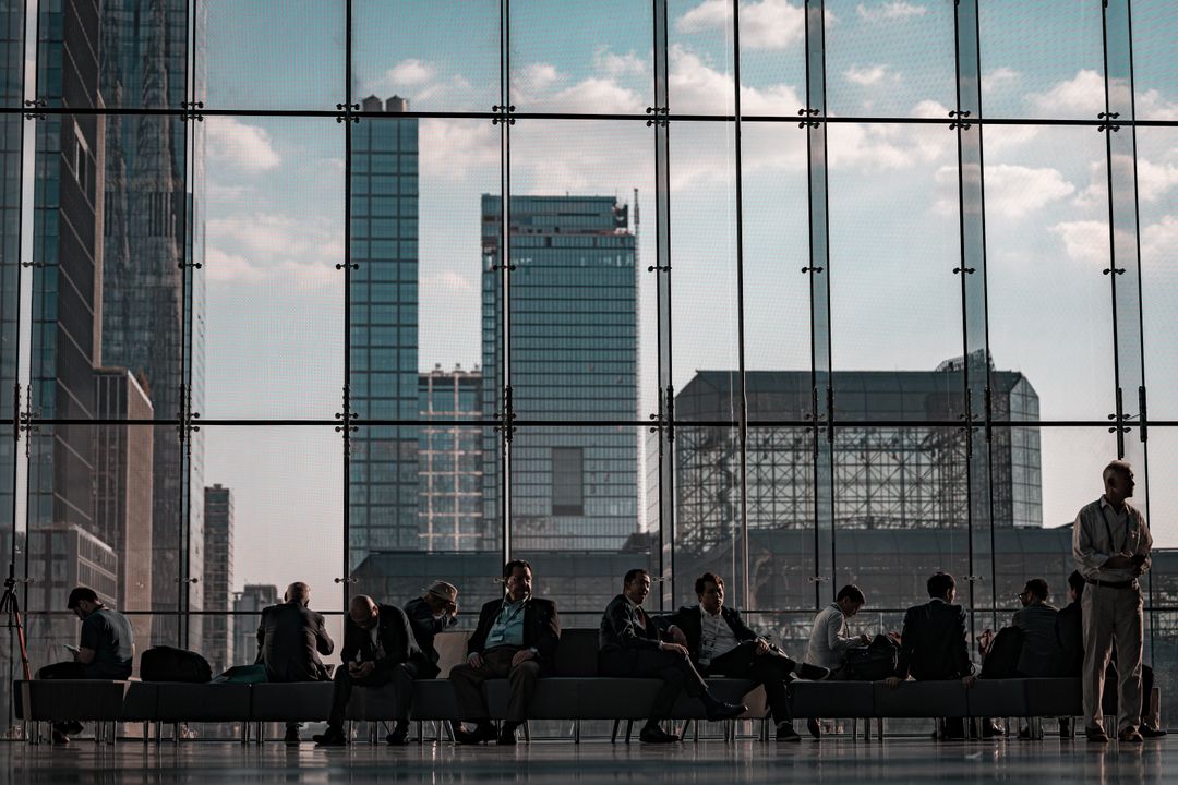 Business professionals seated in a row against a floor-to-ceiling glass curtain wall, with New York City skyscrapers visible behind them.